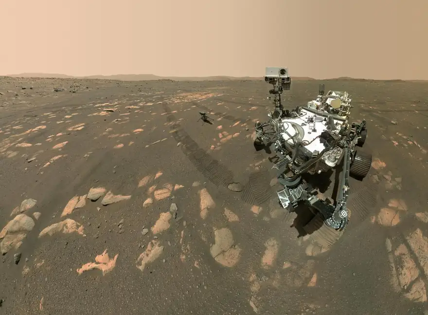 Le rover Perseverance sur le sol rouge et caillouteux de Mars, avec le petit hélicoptère Ingenuity posé au loin.